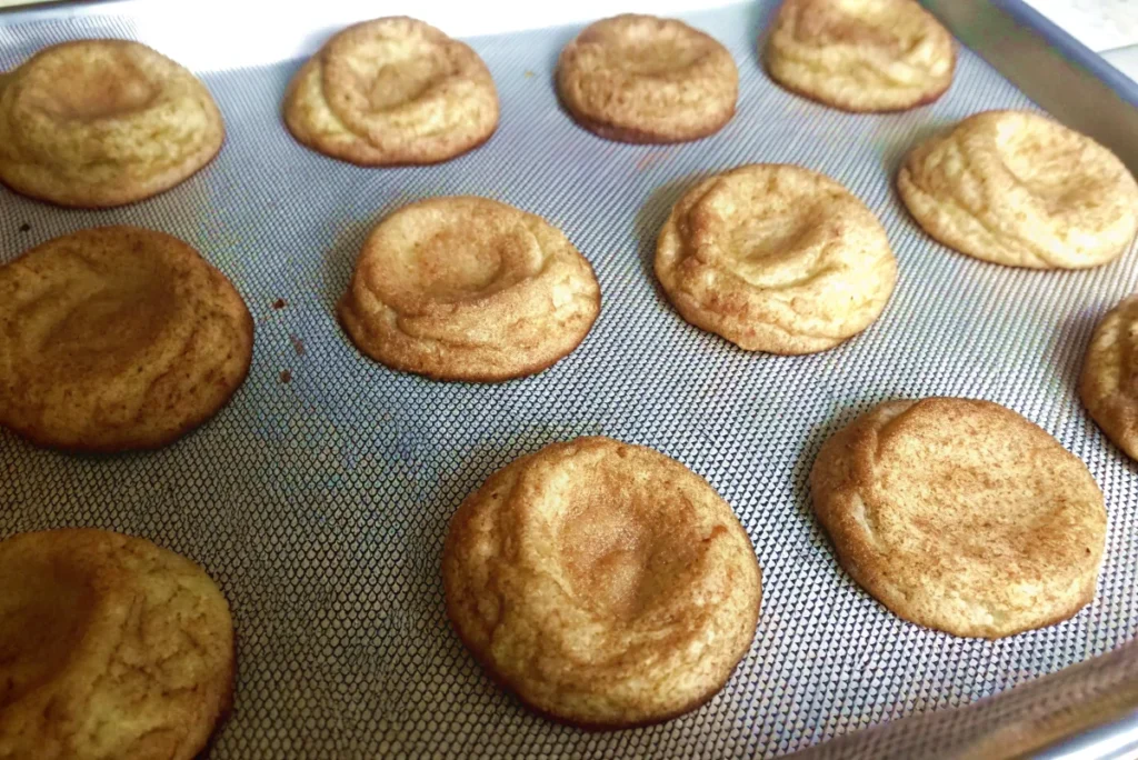 Deflated cookies with sunken centers on a baking sheet lined with a silicone mat.