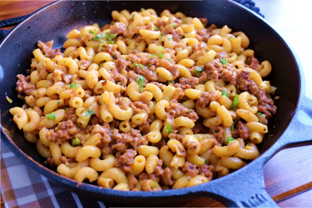 A cast-iron skillet filled with Philly Cheesesteak Pasta, featuring elbow macaroni, seasoned ground beef, and garnished with fresh herbs for a flavorful and comforting meal.
