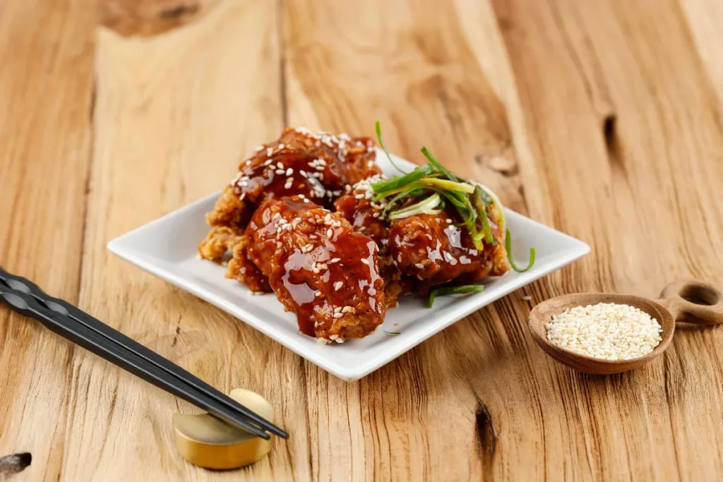 Crispy air fryer teriyaki chicken garnished with sesame seeds and green onions on a white plate.