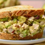 A freshly made tuna avocado sandwich with chunks of tuna, creamy avocado, and red onion between slices of whole-grain bread.